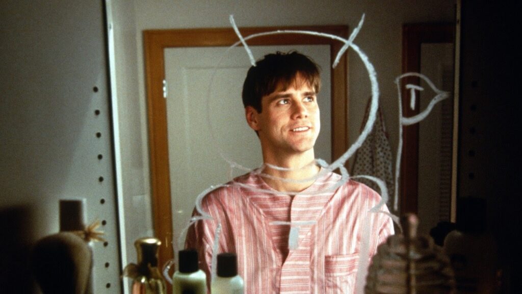 Jim Carrey as Truman Burbank looking into a mirror with drawings on it in "The Truman Show."