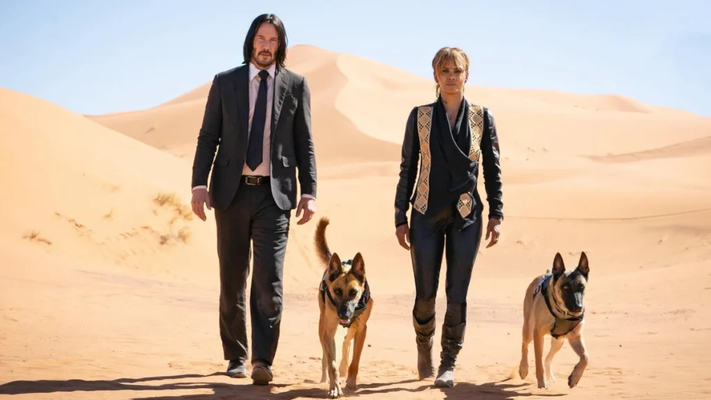 John Wick and Sofia Al-Azwar walking side-by-side with two Belgian Malinois dogs in a sunny desert landscape.