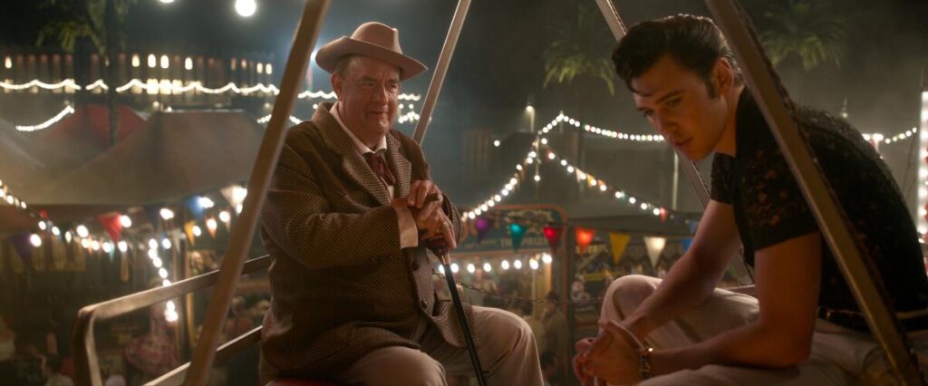 Tom Hanks as Colonel Tom Parker sitting next to Austin Butler as Elvis Presley at a fairground in "Elvis."