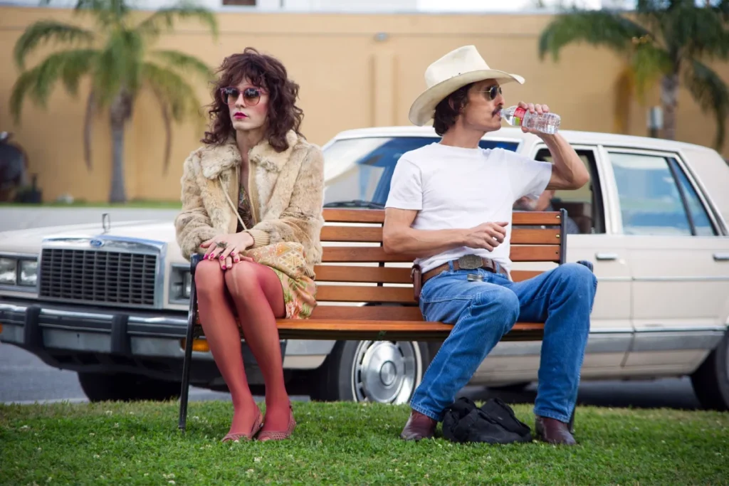 Jared Leto as Rayon and Matthew McConaughey as Ron Woodroof, sitting on a park bench with a vintage car in the background, in "Dallas Buyers Club."